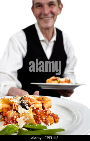 A servant is holding a plate with pasta, tomato sauce, parmesan cheese and basil. Focus on plate. Close-up. Stock Photo