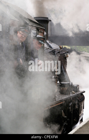 Steam train driver looking back waiting permission to leave with his train recreating a travel scene commonly seen in the 1940s, 1950s and 196 Stock Photo