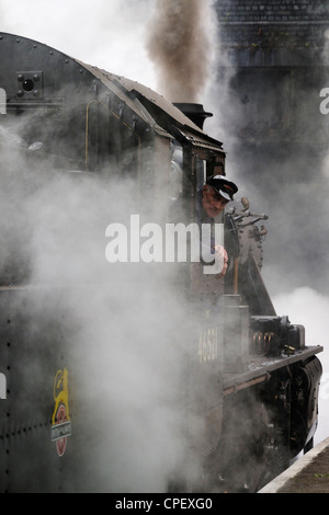 Steam train driver looking back waiting permission to leave with his train recreating a travel scene commonly seen in the 1940s, 1950s and 1960s Stock Photo