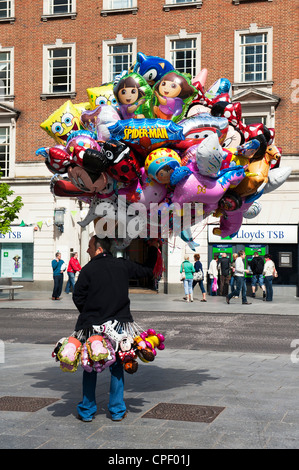 Balloon seller holding character helium balloons on the streets of Exeter, England Stock Photo