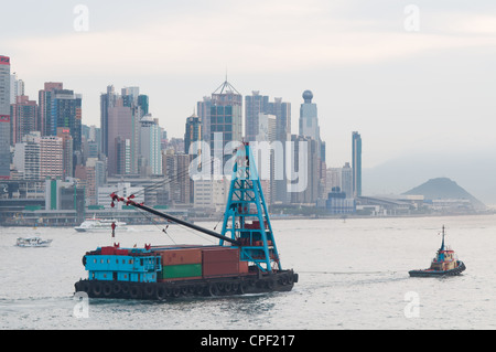 Barge with containers being towed during early evening hours in Hong Kong. The skyline of Hong Kong Island in the background. Stock Photo