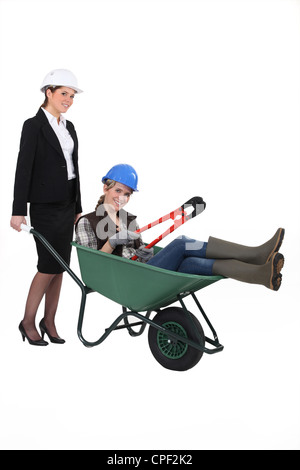 A professional woman pushing a blue collar worker in a wheelbarrow Stock Photo