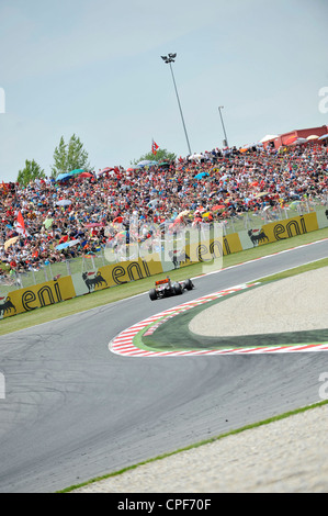 race car passes through curve in front of grandstand filled with ...