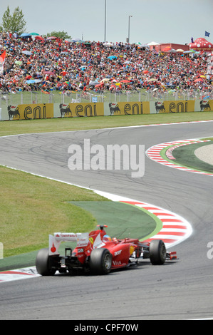 race car passes through curve in front of grandstand filled with ...