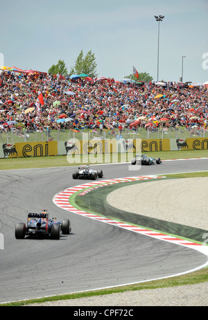 three race cars pass through curve in front of grandstand filled with ...