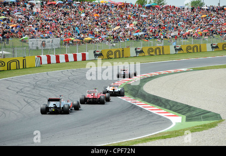 four race cars pass through curve in front of grandstand filled with ...