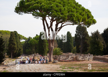 Tourists shading under a plane tree on the Decumanus   whilst being lectured to by their leader at The ancient roman port town ruin of Ostia near Rome Stock Photo