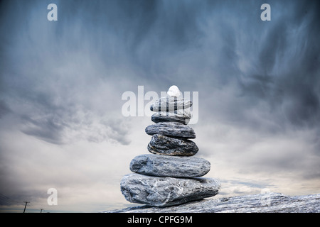 Stone cairn in front of stormy sky and a few utility poles. Concepts of global problems ahead, and finding a direction. Stock Photo