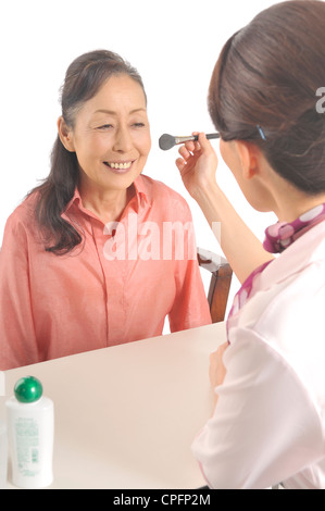 Mid adult woman doing senior woman's makeup Stock Photo