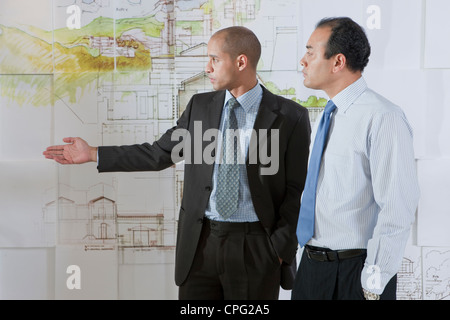 Two businessmen discussing blueprints on the wall. Stock Photo