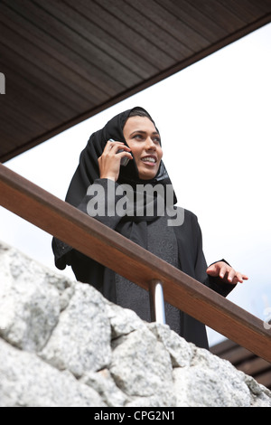 Arab woman using mobile phone in the balcony, smiling. Stock Photo