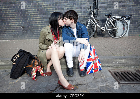 A young couple sitting on a kerb kissing, Spitalfield, London, England, UK Stock Photo