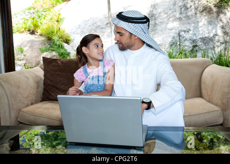 Arab father and daughter with laptop, sitting on sofa. Stock Photo