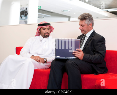 Two businessmen using laptop, sitting in office lobby. Stock Photo