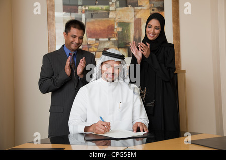 Arab businessman signing document, two colleague clapping on the side. Stock Photo