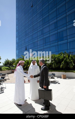 Three businessmen shaking hands in front of building. Stock Photo