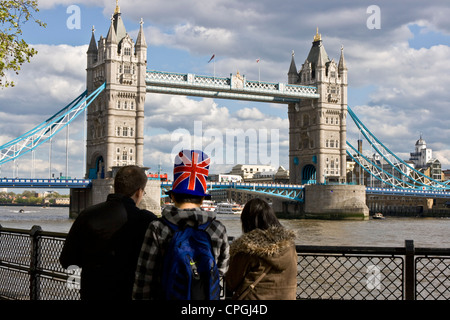 Boy holidaymaker wearing Union Jack top hat patriotic headgear looking at grade 1 listed Tower Bridge London England Europe Stock Photo