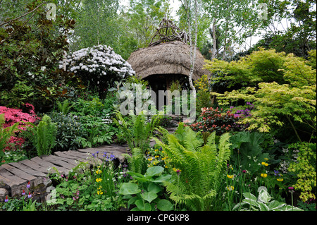 Mature show garden with thatch roofed hut at the RHS Chelsea flower show 2012 Stock Photo