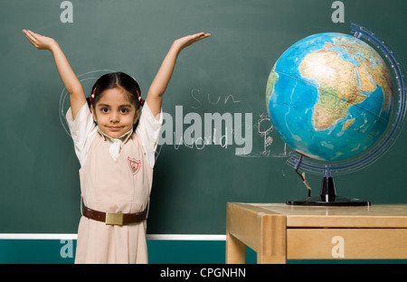 Girl (6-7) standing by board, arms raised, portrait Stock Photo