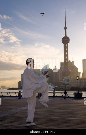 Man in white uniform doing Tai Chi exercises on the Bund at dawn with Pearl Tower in Shanghai China Stock Photo