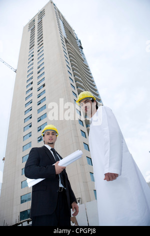 Businessmen standing with blueprints by building, low angle view, portrait Stock Photo