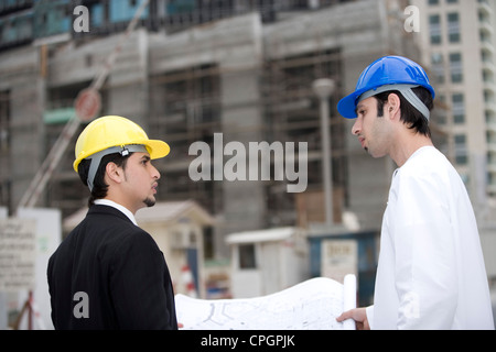 Businessmen discussing blueprints at construction site, side view Stock Photo