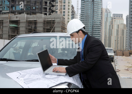 Businessman wearing hard hat using laptop, side view Stock Photo
