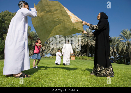 Mother with children spreading sheet on grass while father with son standing in background Stock Photo
