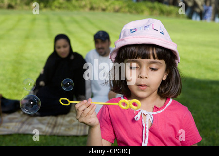 Girl holding bubble wand while parents sitting in background Stock Photo