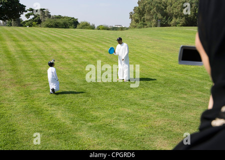 Father and son playing with plastic disk at park while woman taking photograph Stock Photo