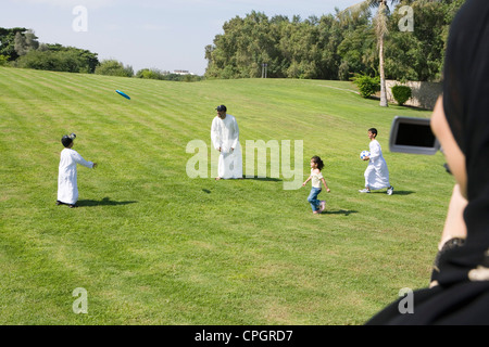 Father playing with children at park while woman taking photograph Stock Photo