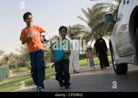 Boys holding football and plastic disk while parents with daughter standing in background Stock Photo