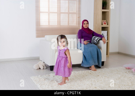 Mother holding the television remote control, daughter watching Stock Photo