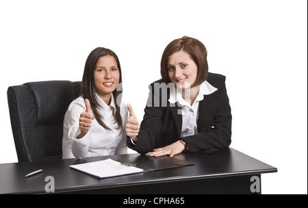 Two positive businesswomen colleagues with thumbs up at the office table against a white background. Stock Photo