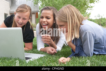 Three girls laugh at a funny internet video on a laptop outdoors. Stock Photo