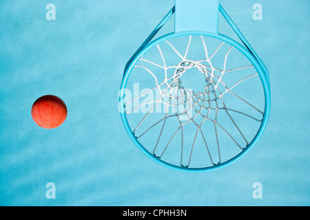 A basketball is floating in a swimming pool next to a view of the basketball hoop. Overhead viewpoint of hoop, net and ball. Stock Photo