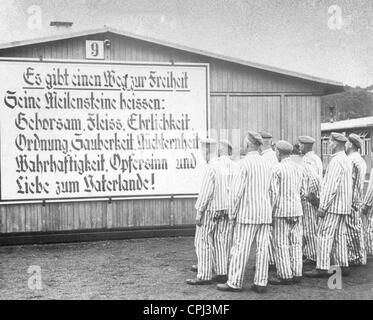 Camp internees in striped uniforms at Sachsenhausen concentration camp standing before a sign with a National Socialist slogan, Stock Photo