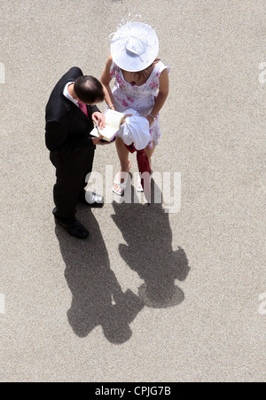 A man and an elegantly dressed woman wearing a fancy hat at horse races, Ascot, UK Stock Photo