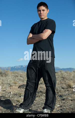 Athletic Hispanic young man standing with arms folded outside in the middle of the desert wearing workout clothing. Stock Photo