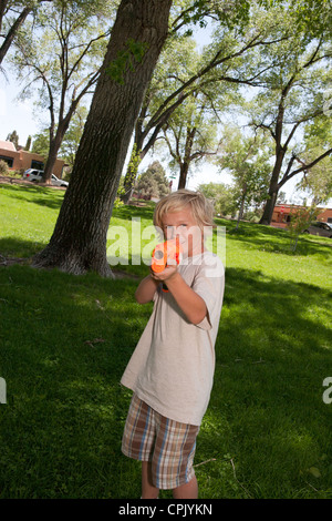 Ten year old boy holding a plastic nerf gun at a park, pointed at camera. Stock Photo