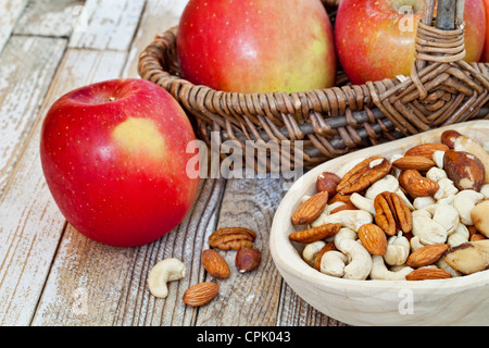 red apples and nuts (cashew, walnut, almond, Brazilian) in rustic setting (primitive wooden bowl and wicker basket Stock Photo