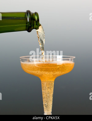 A bottle of apple cider being poured into a glass. The background is fading gray, which makes the colors stand out. Stock Photo