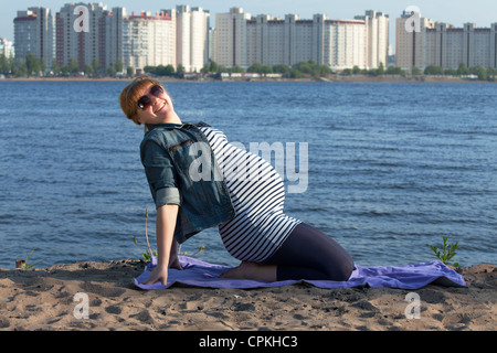 Pregnant woman doing gymnastic exercises on the river coast Stock Photo