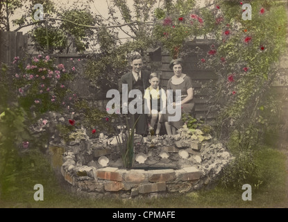 1920's original tinted black and white photograph of familydressed in their smart Sunday Best clothes,  posing proudly next to their garden pond in Southend-on-Sea, Essex, England, UK  circa 1922 Stock Photo