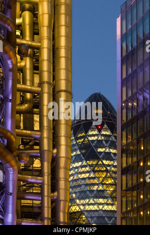 The Swiss Re building - aka the Gherkin - at night, foregrounded by the Lloyds Building Stock Photo