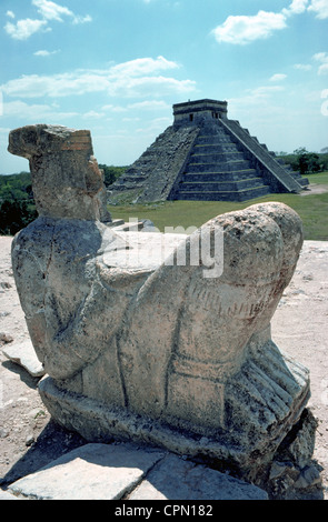 A stone statue of Chac-Mool looks toward the Castle of Kukuclan step-pyramid in the Mayan ruins of Chichen Itza on the Yucatan Peninsula in Mexico. Stock Photo