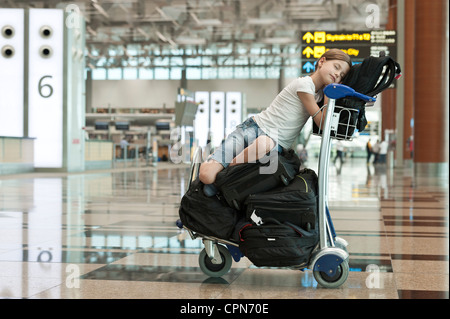 Girl resting on top of luggage cart in airport Stock Photo