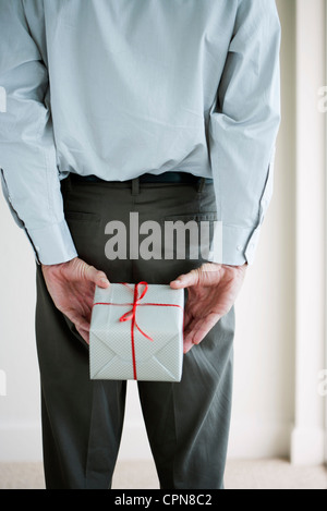 Man holding wrapped gift behind his back, cropped Stock Photo