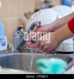 Washing of the dishes - woman hands rinsing dishes under running water in the sink Stock Photo