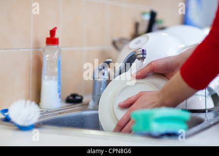 Washing of the dishes - woman hands rinsing dishes under running water in the sink Stock Photo